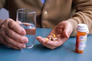 Hands holding a glass of water and pills